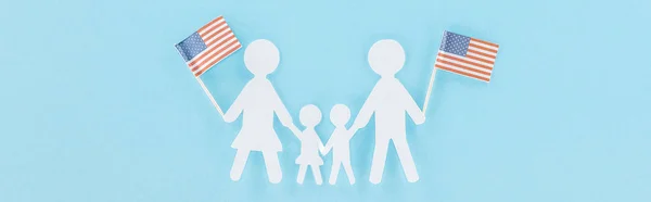 Panoramic shot of paper cut family holding decorative american flags on wooden sticks on blue background — Stock Photo