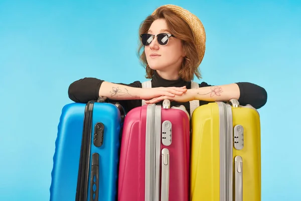 Smiling girl in sunglasses and straw hat looking away near multicolored travel bags isolated on blue — Stock Photo