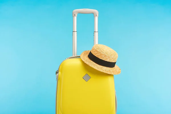 Жовта дорожня сумка з солом'яним капелюхом ізольована на синьому — стокове фото