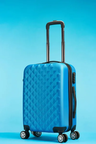 Синий чемодан с ручкой на колесах на синем фоне — стоковое фото