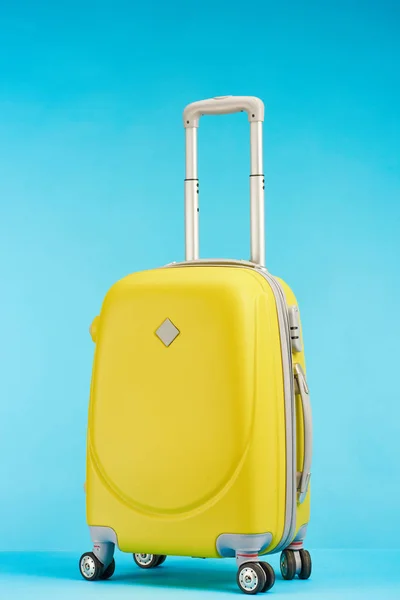 Yellow colorful travel bag with handle on wheels on blue background — Stock Photo