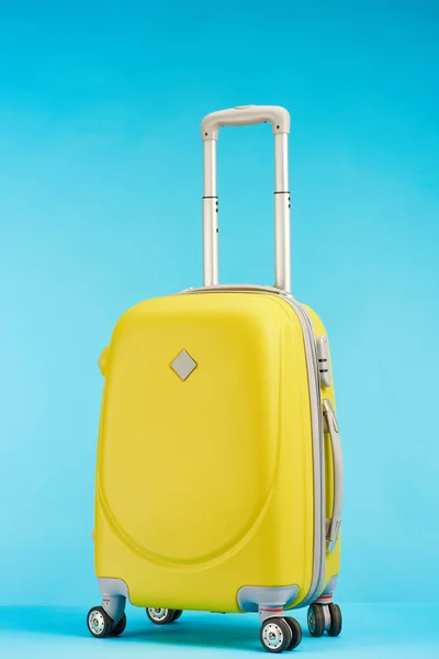 Sac de voyage coloré jaune avec poignée sur roues sur fond bleu — Photo de stock