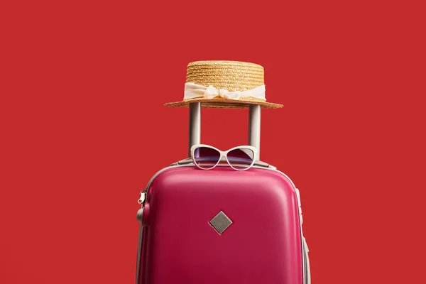 Rote bunte Reisetasche mit Strohhut und Sonnenbrille isoliert auf rot — Stockfoto