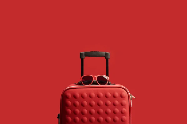 Red colorful textured travel bag with sunglasses isolated on red — Stock Photo