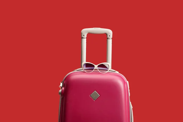 Red colorful travel bag with sunglasses isolated on red — Stock Photo