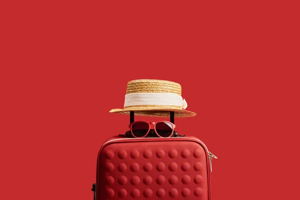 Bolsa de viaje roja con sombrero de paja y gafas de sol aisladas en rojo - foto de stock