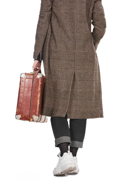 Вид женщины в клетчатом пальто, держащей винтажный выветриваемый чемодан, изолированный на белом — стоковое фото
