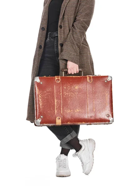 Cropped view of woman in plaid coat with crossed legs holding vintage weathered suitcase isolated on white — Stock Photo