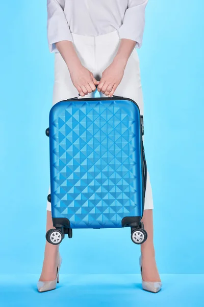 Vista recortada de la mujer sosteniendo maleta azul sobre fondo azul - foto de stock
