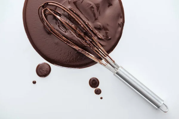 Top view of balloon whisk with circle of melted chocolate on white background — Stock Photo