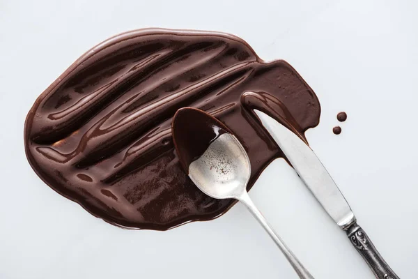 Вид сверху разлитого растопленного шоколада столовым ножом и ложкой — стоковое фото