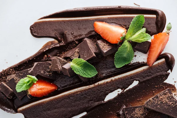 Top view of melted chocolate with pieces of chocolate bar, strawberries and green mint — Stock Photo