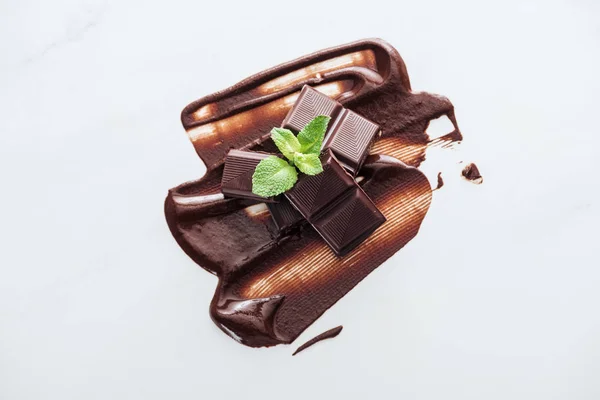 Vista superior de trozos de barra de chocolate y menta fresca sobre fondo blanco - foto de stock