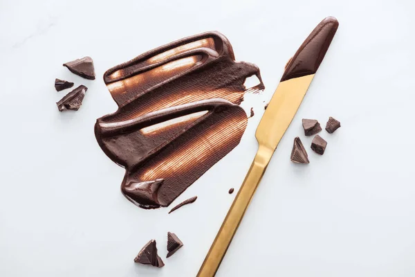 Vista superior del cuchillo de mesa de oro con chocolate líquido y trozos de chocolate - foto de stock