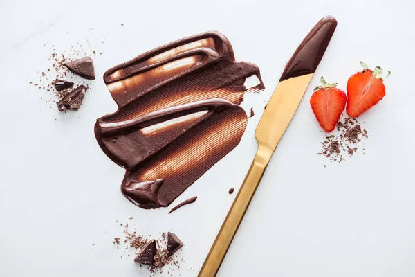 Top view of gold table knife with strawberries, liquid chocolate, pieces of chocolate bar and cocoa powder — Stock Photo
