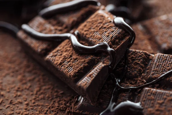 Vista da vicino di pezzi di barretta di cioccolato fondente con cioccolato liquido e cacao in polvere — Foto stock