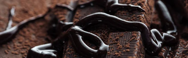Panoramaaufnahme von geschmolzener Schokolade mit Stücken von dunkler Schokolade und Kakaopulver — Stockfoto