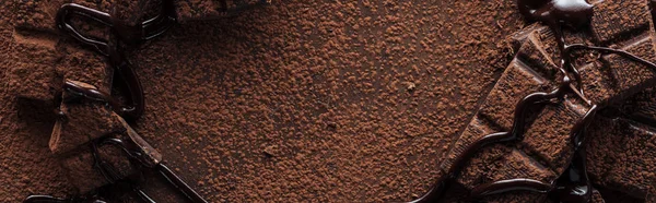 Panoramic shot of pieces of chocolate bar with melted chocolate and cocoa powder — Stock Photo