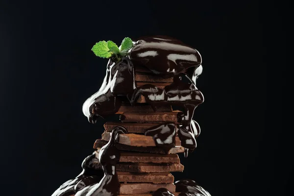 Dark chocolate stack with melted chocolate and fresh mint isolated on black — Stock Photo