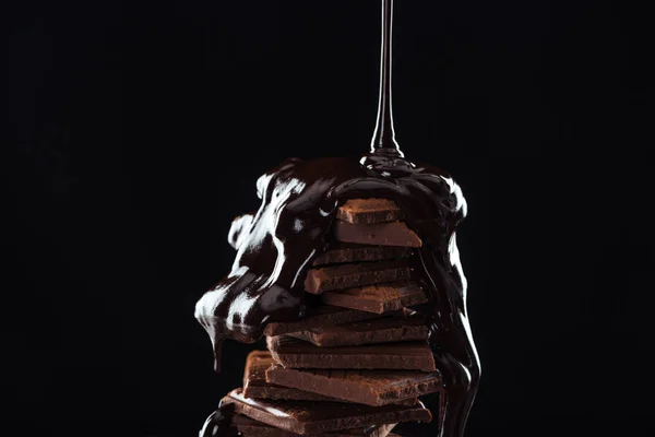 Hot melted chocolate pouring on chocolate stack, isolated on black — Stock Photo