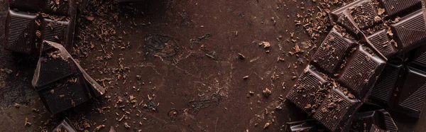 Panoramische Aufnahme dunkler Schokoladenriegel mit Schokoladenstücken auf Metallhintergrund — Stockfoto