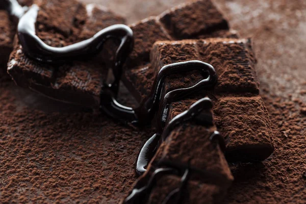 Selective focus of pieces of chocolate bar with melted chocolate and cocoa powder on metal background — Stock Photo