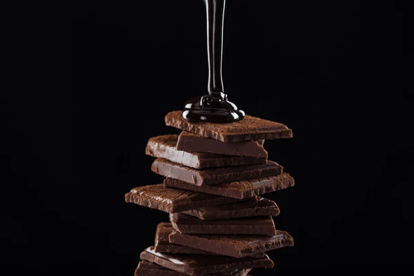 Chocolat noir fondu à chaud versant sur la pile de chocolat, isolé sur noir — Photo de stock