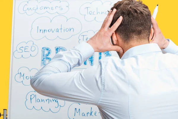 Back view of businessman standing near white office board with words, holding hands on head — Stock Photo