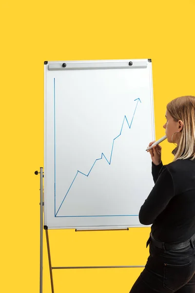 Rückansicht einer Geschäftsfrau, die neben weißem Flipchart steht, Wachstumsgrafik betrachtet, isoliert auf gelb steht — Stockfoto