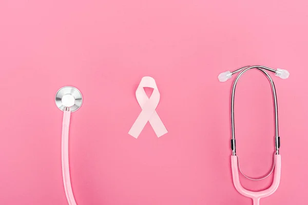 Vue du dessus du stéthoscope et du symbole rose du cancer du sein sur fond rose — Photo de stock