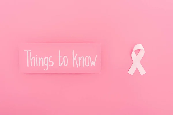 Vista dall'alto della scheda con le cose da sapere lettering e il segno del cancro al seno su sfondo rosa — Foto stock
