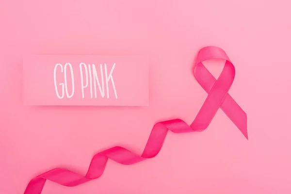 Vista dall'alto della scheda con andare rosa lettering e nastro cremisi cancro al seno su sfondo rosa — Foto stock