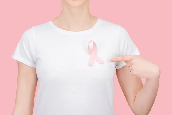 Частичный вид женщины в белой футболке, указывающей пальцем на розовый знак рака молочной железы, выделенный розовым — стоковое фото