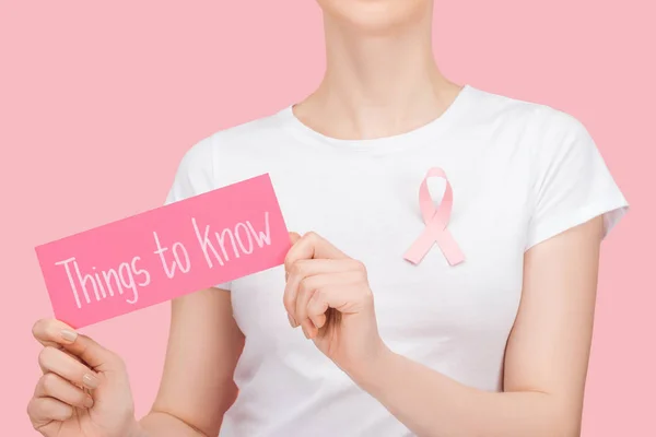 Abgeschnittene Ansicht von Frau mit rosa Brustkrebs Zeichen hält rosa Karte mit Dingen zu wissen Schriftzug isoliert auf rosa — Stockfoto