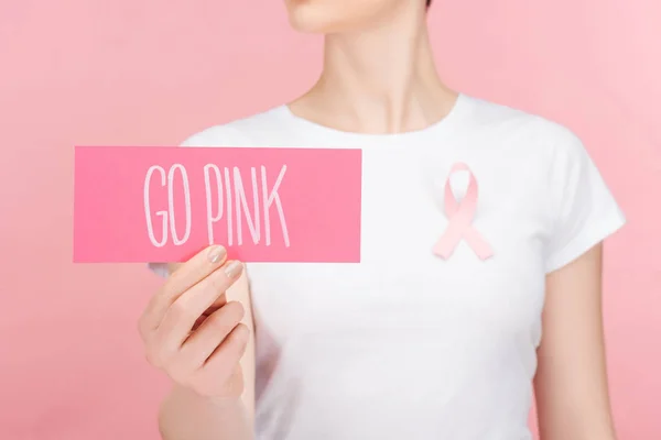 Foco seletivo da mulher com sinal de câncer de mama rosa segurando cartão rosa com letras go rosa isolado no rosa — Fotografia de Stock