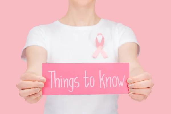 Selective focus of woman with pink breast cancer sign holding pink card with things to know lettering isolated on pink — Stock Photo