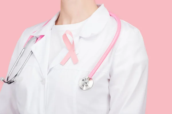 Partial view of doctor in white coat with pink breast cancer sign and stethoscope isolated on pink — Stock Photo