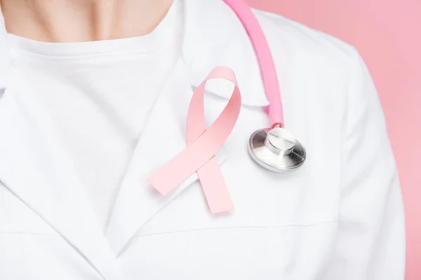 Vista de cerca del médico de bata blanca con signo de cáncer de mama rosa y estetoscopio aislado en rosa - foto de stock