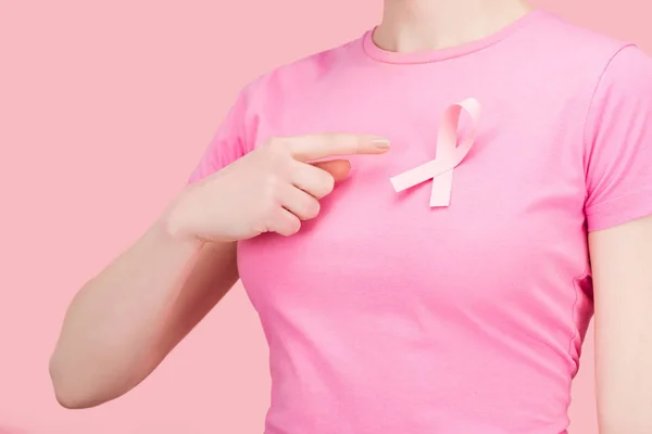 Partial view of woman in pink t-shirt pointing with finger at silk breast cancer sing isolated on pink — Stock Photo