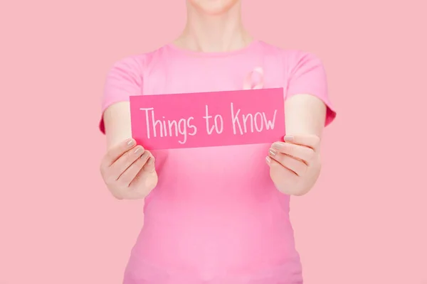 Selective focus of woman in pink t-shirt holding card with things to know lettering isolated on pink, breast cancer concept — Stock Photo