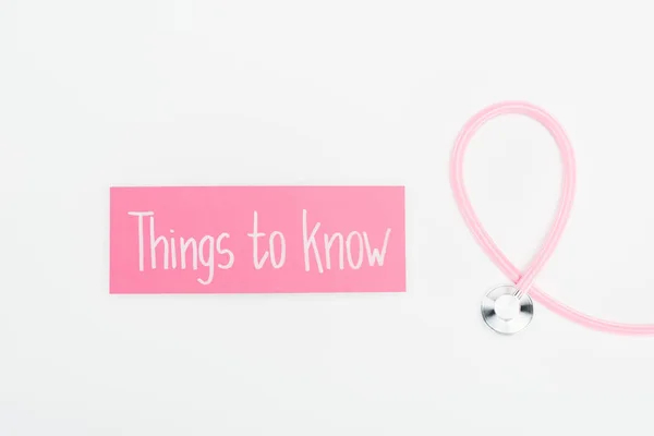 Draufsicht auf Stethoskop und rosa Karte mit Wissenswertem Schriftzug auf weißem Hintergrund — Stockfoto