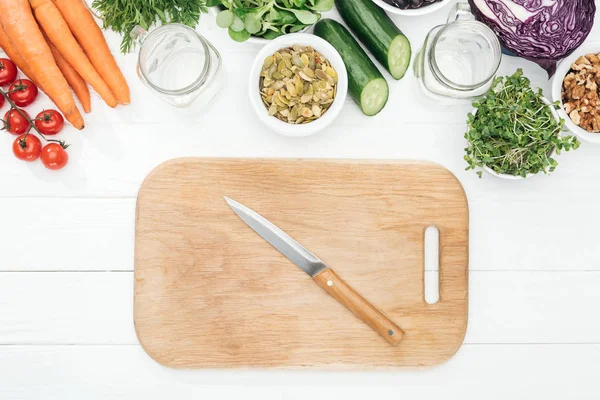 Vista dall'alto di frutta e verdura vicino a vasi di vetro, coltello e tagliere su tavolo bianco in legno con spazio copia — Foto stock