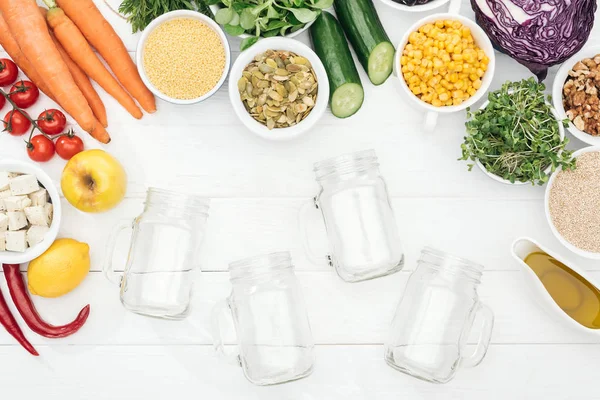 Vue de dessus des fruits et légumes près des bocaux en verre vides sur la table blanche en bois avec espace de copie — Photo de stock