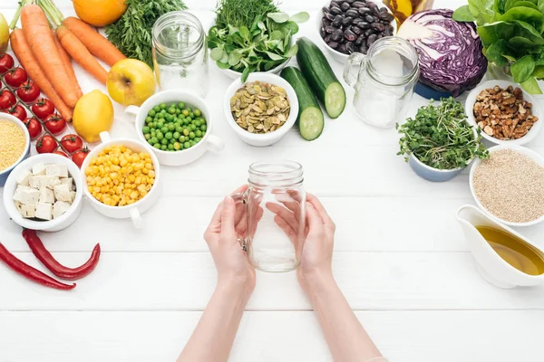 Cropped view of woman holding empty glass jar on wooden white table — Stock Photo