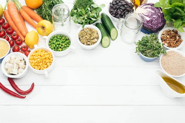 Vista superior de frutas e legumes orgânicos perto de frascos de vidro na mesa branca de madeira com espaço de cópia — Fotografia de Stock