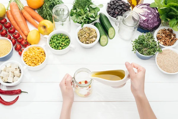 Cropped view of woman pouring oil in glass jar on wooden white table — Stock Photo