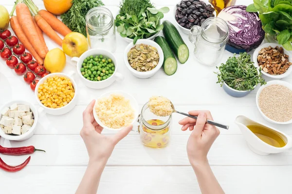 Cropped view of woman adding couscous to glass jar on wooden white table — Stock Photo