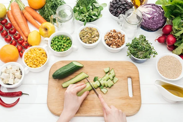 Vista recortada de mujer cortando pepino en mesa blanca de madera - foto de stock