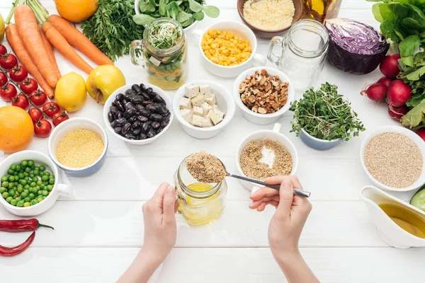 Vista recortada de la mujer agregando semillas en frasco de vidrio con ensalada en mesa blanca de madera — Stock Photo