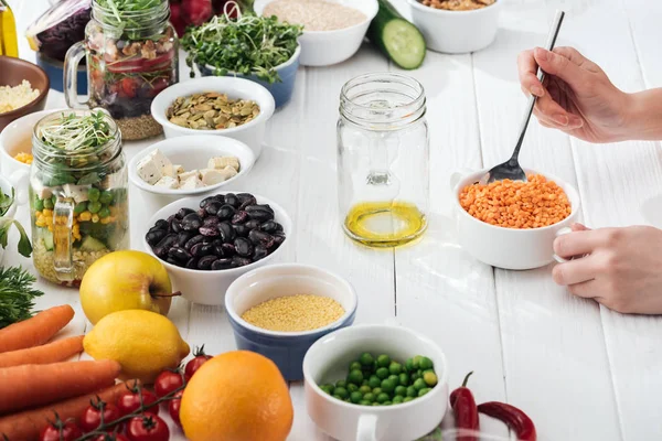 Vue recadrée de la femme ajoutant du couscous dans un bocal en verre sur une table blanche en bois — Photo de stock